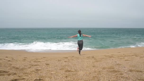 Chica feliz corre a lo largo de la playa de ida y vuelta. Orilla desierta del Océano Atlántico en Portugal. Movimiento lento — Vídeo de stock