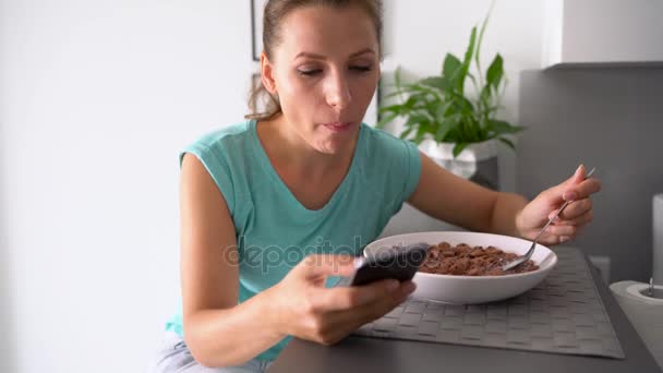 Mujer utiliza un teléfono inteligente mientras come su desayuno — Vídeos de Stock