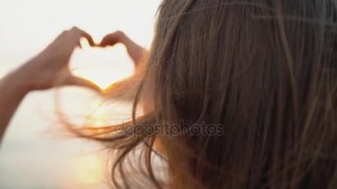 Kadın kalp sembol elleri günbatımı sırasında kumsalda yapma. Ağır çekim