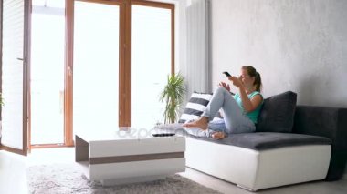 Kanepede yatan ve Tv seyretmek genç, güzel bir kadın. O uzaktan kumanda üzerindeki anahtarları süresiz olarak, izleme atış