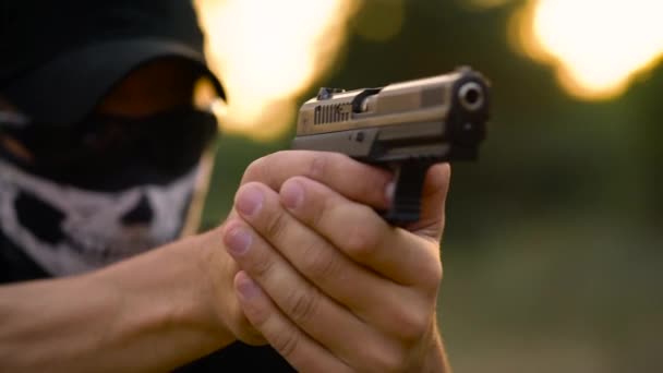 Homem com o rosto fechado com um lenço e óculos de sol se preparando para atirar uma arma, de perto — Vídeo de Stock