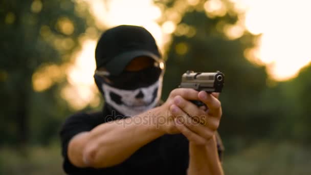 Hombre con la cara cerrada con un pañuelo y gafas de sol preparándose para disparar un arma, de cerca — Vídeos de Stock