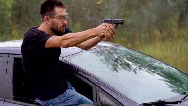 Genç adam arabayı pencereden yaslanmış bir silahtan ateş ediyor, yakın çekim — Stok video