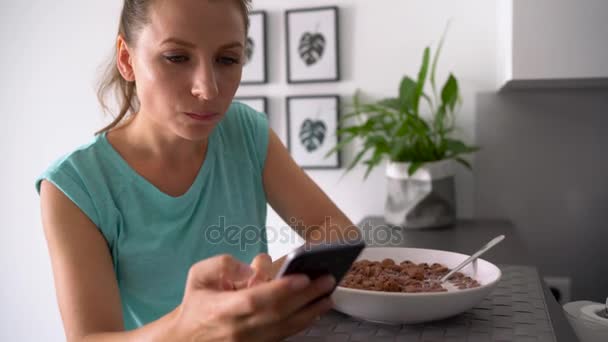 Mujer utiliza un teléfono inteligente mientras come su desayuno — Vídeo de stock