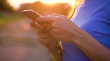 Kadın bir akıllı telefon açık havada günbatımında kullanarak güneş gözlüğü