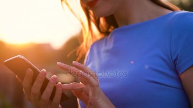 Kadın bir akıllı telefon açık havada günbatımında kullanarak güneş gözlüğü