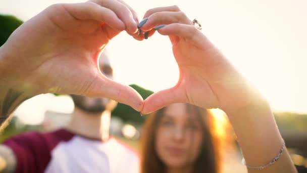 Молода пара закохана у створення символу серця руками під час заходу сонця. Повільний рух — стокове відео