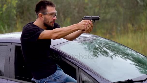 Молодий чоловік стріляє з пістолета, визираючи з вікна машини, крупним планом — стокове відео