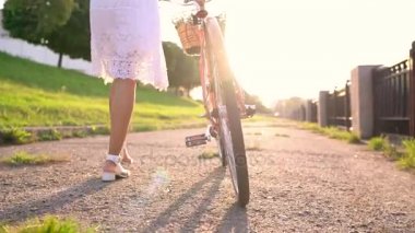 Günbatımında bir bisiklet ile yürüyen genç güzel kadın. Ağır çekim