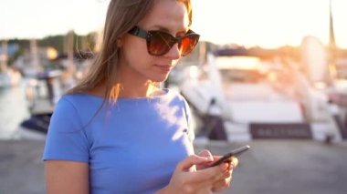 Kadın güneş gözlüğü smartphone kullanarak süre yürüyen bir dock yat ve tekne batımında yakın bir sürü ile aşağı yukarı, yakın çekim. Ağır çekim