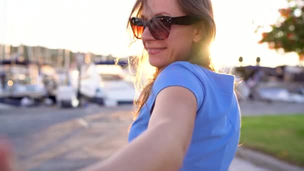 Suivez-moi - heureuse jeune femme en lunettes de soleil tirant les gars main. Main dans la main marchant à la marina avec beaucoup de yachts et de bateaux, près. Mouvement lent — Video