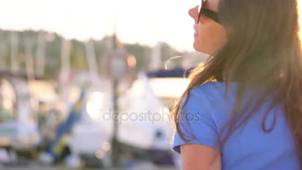 Donna in occhiali da sole a piedi lungo il molo con un sacco di yacht e barche al tramonto, da vicino. Rallentatore — Video Stock