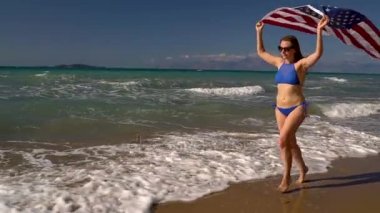 Bikini kadın bizimle bayrağı sahilde su çalışan plaj. Bağımsızlık günü ABD kavramı. Ağır çekim