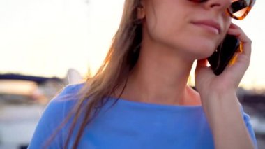 Kadın bir dock yat ve tekne günbatımı, yakın çekim, bir sürü ile aşağı yürürken smartphone kullanarak güneş gözlüğü. Ağır çekim