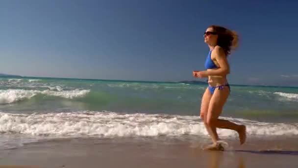 Bikini de playa mujer despreocupada corriendo por el agua en la playa. Pintoresca costa marítima de Corfú, Grecia — Vídeo de stock