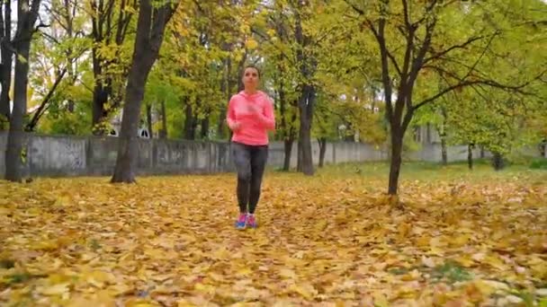 Nahaufnahme einer Frau, die bei Sonnenuntergang durch einen herbstlichen Park läuft. Zeitlupe — Stockvideo