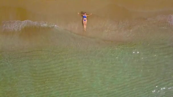 Toma aérea de una mujer en bikini acostada en una playa de arena y las olas lavan sus pies — Vídeos de Stock