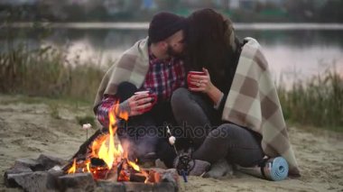 Şenlik ateşinde göl çevresinde oturan, söz ve içme aşık çift sıcak çay