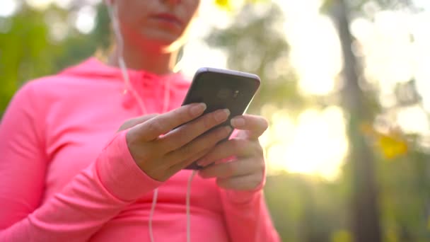 Frau mit Kopfhörer und Smartphone wählt die Musik für einen Lauf durch den Herbstpark — Stockvideo