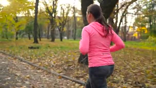 Close up of woman with headphones and smartphone running through an autumn park at sunset — Stock Video