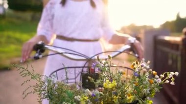 Çiçekler yakın çekim sepetle. Gün batımında Onun Bisiklet duran kadın.