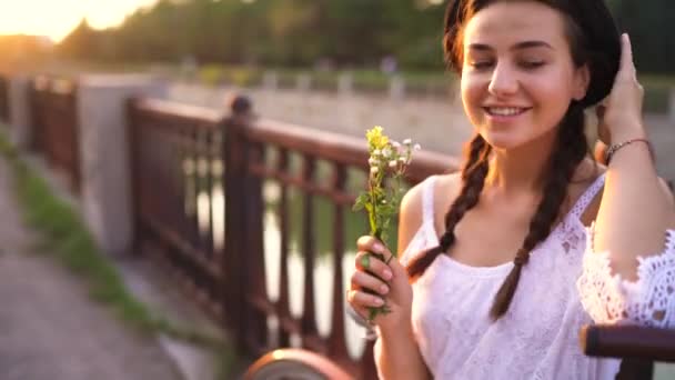 Νεαρή όμορφη γυναίκα που κάθεται με το ποδήλατο με λουλούδια στο ηλιοβασίλεμα — Αρχείο Βίντεο