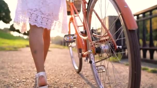 Jonge mooie vrouw lopen met een fiets bij zonsondergang. Slow motion — Stockvideo