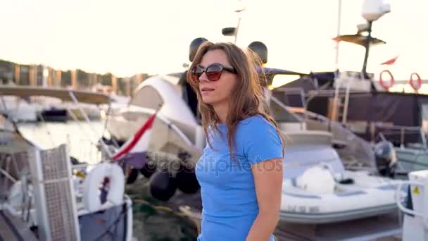 サングラスの日没で、多くのヨットやボートとドックを歩いて女性をクローズ アップ。スローモーション — ストック動画