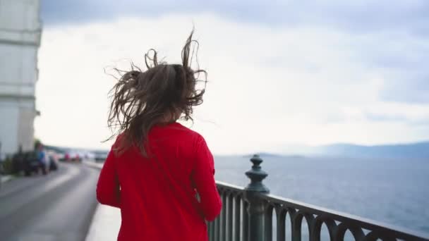 Женщина в красном платье бежит вдоль набережной на морском побережье. Медленное движение — стоковое видео