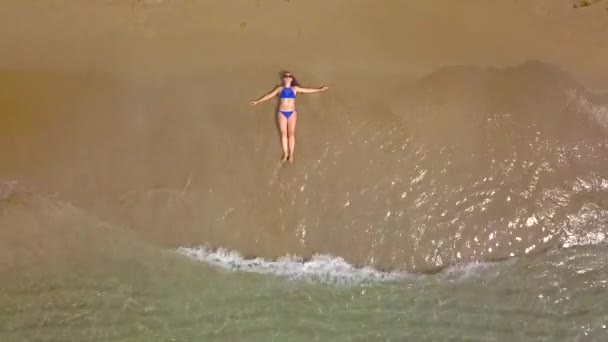 Tiro aéreo de uma mulher em um biquíni deitado em uma praia de areia e ondas lavar os pés — Vídeo de Stock