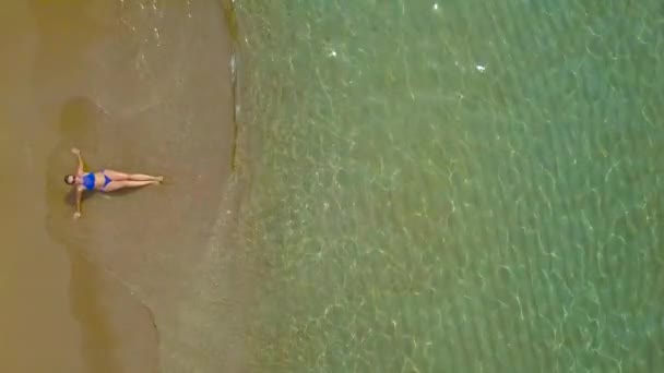 Toma aérea de una mujer en bikini acostada en una playa de arena y las olas lavan sus pies — Vídeo de stock