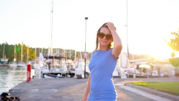 Femme en lunettes de soleil marchant le long du quai avec beaucoup de yachts et bateaux au coucher du soleil, gros plan — Video