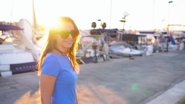 Mujer en gafas de sol caminando por el muelle con una gran cantidad de yates y barcos al atardecer, de cerca — Vídeos de Stock