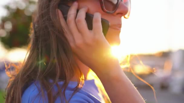 Жінка в сонцезахисних окулярах, використовуючи смартфон, ходячи по причалу з великою кількістю яхт і човнів на заході сонця, крупним планом — стокове відео