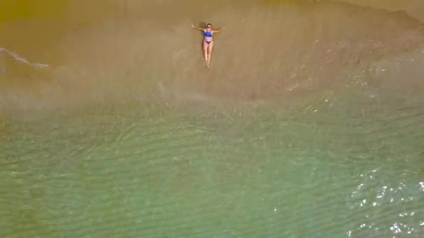 Aerial shot of a woman in a bikini lying on a sandy beach and waves wash her feet — Stock Video