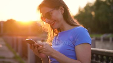 Kadın bir akıllı telefon açık havada günbatımında kullanarak güneş gözlüğü