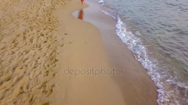 Vista superior de uma mulher andando descalça ao longo da praia de areia molhada. Onda a correr está a lavar as pegadas na areia — Vídeo de Stock