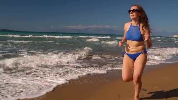 Bikini de playa mujer despreocupada corriendo por el agua en la playa. Pintoresca costa marítima de Corfú, Grecia — Vídeo de stock