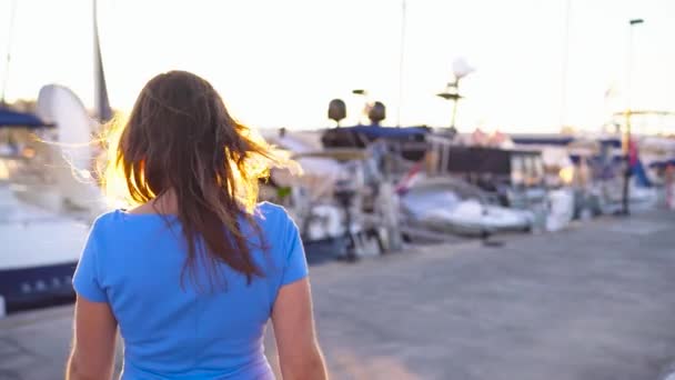 Femme en lunettes de soleil marchant le long du quai avec beaucoup de yachts et bateaux au coucher du soleil, fermer. Mouvement lent — Video