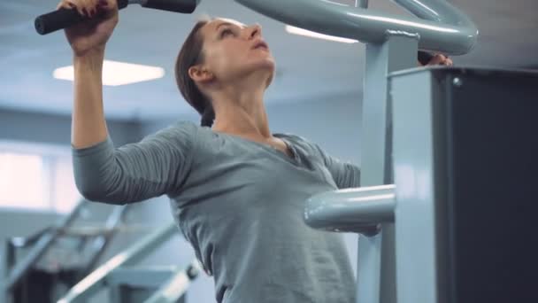 Woman does pull-ups on gravitron for strengthening the shoulder muscles in the gym — Stock Video