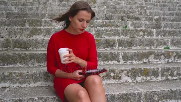 Woman reading an e-book sitting on the steps outdoors — Stock Video