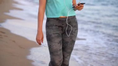 Sahilde yürüyüş kulaklık atletik kadınla. Video farklı hızlarda - normal ve yavaş