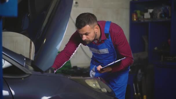 Serviço de carro, reparação, manutenção e conceito de pessoas - mecânico verifica a qualidade do trabalho realizado — Vídeo de Stock