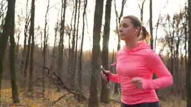 Kadının bir sonbahar orman günbatımında çalışan akıllı telefon ve kulaklık ile yakın çekim