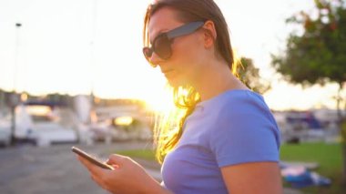 4 in 1 video. Kadın bir dock yat ve tekne günbatımı, yakın çekim, bir sürü ile aşağı yürürken smartphone kullanarak güneş gözlüğü. Ağır çekim