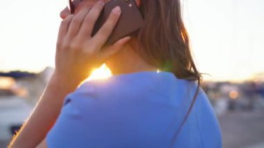 Kadın bir dock yat ve tekne günbatımı, yakın çekim, bir sürü ile aşağı yürürken smartphone kullanarak güneş gözlüğü
