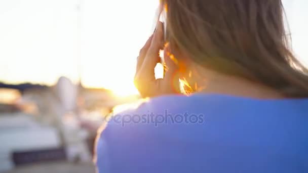 Wideo 2 w 1. Kobieta w okulary za pomocą smartfona podczas spaceru dół dock z dużą ilością jachtów i łodzi w zachód słońca, zbliżenie — Wideo stockowe
