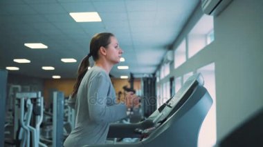 Spor salonunda koşu bandı üzerinde çalışan kadın. Ağır çekim