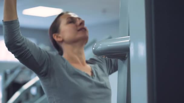 Женщина делает подтягивания на гравитроне для укрепления мышц плеча в тренажерном зале — стоковое видео