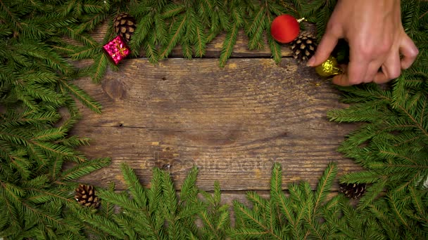 Womens händerna skapa en jul inredning. Julgran grenar med kottar och julpynt på trä textur redo för din design — Stockvideo